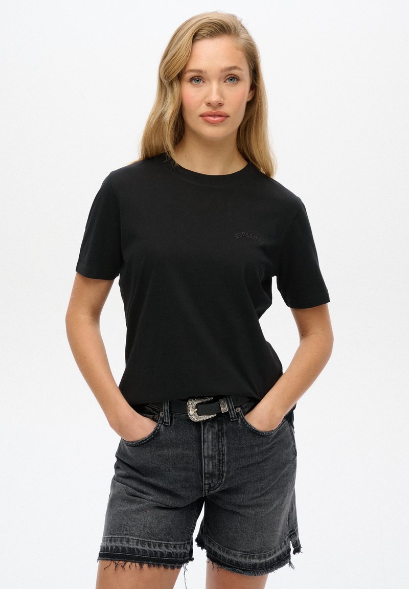 Zwarte katoenen T-shirt met korte mouwen, ronde hals, subtiele branding, gecombineerd met donkere denim shorts met een gefranje zoom en een riem.