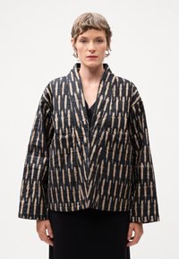 Jachetă neagră matlasată cu un model unic crem, având un design structurat, mâneci largi și guler tip șal.