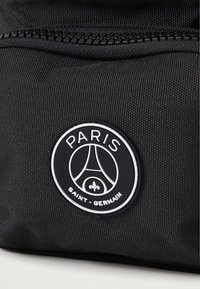 Černý textilní pouzdro s texturovaným povrchem, se zipovým uzavřením a kulatým logem s nápisem "Paris Saint-Germain" v bílé barvě.