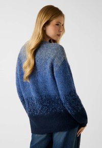 Blauwe gebreide trui met een verloopontwerp, waarbij de kleur overgaat van lichtblauw naar donker marineblauw aan de onderkant. Zachte textuur en losse pasvorm.