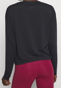 Black long-sleeve shirt with a loose fit and rounded hem, paired with form-fitting dark pink leggings. The fabric appears smooth and soft.