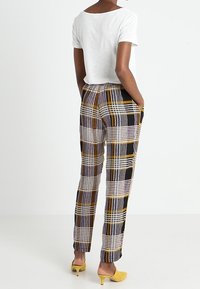 Rutiga byxor i svart, gult och lila; lättviktig tyg med resårmidja; matchas med en vit t-shirt med kort ärm.