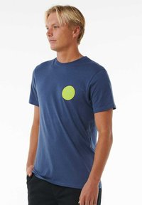Camiseta de algodón azul marino con un gráfico redondo en neón verde en el lado izquierdo del pecho. Mangas cortas y cuello redondo, ajuste relajado.