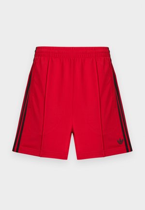 Punased spordipüksid elastse vöökohaga, millel on mustad küljeribad ja väike must logo alumisel vasakul esiküljel. Sile tekstuur.