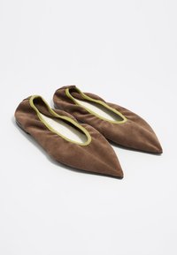 Zapatos planos de ante marrón con punteras puntiagudas, ribete elástico verde alrededor de la abertura y suela negra lisa. Textura suave, diseño sencillo.