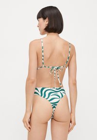 Bikini z nastavljivimi črtastimi naramnicami, z zeleno-belo vijugasto vzorcem, zavezovanjem na hrbtu in nizkim krojem na bikiniju.