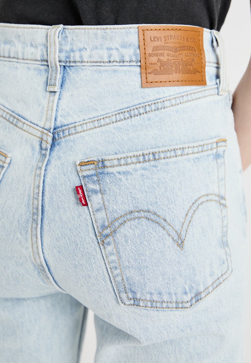 Jeans de mezclilla azul claro con un parche de cuero etiquetado "Levi Strauss & Co." y una etiqueta roja en el bolsillo trasero; presenta un detalle de costura curva.