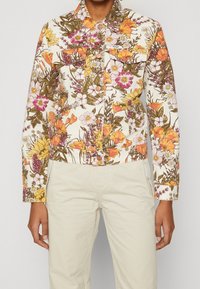 Giacca di jeans floreale con base bianca, caratterizzata da motivi floreali colorati in rosa, arancione e giallo. Include dettagli con bottoni e colletto.