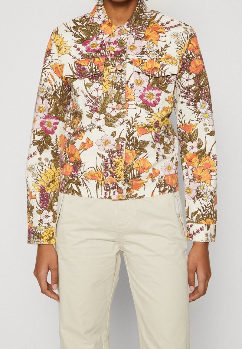 Giacca di jeans floreale con base bianca, caratterizzata da motivi floreali colorati in rosa, arancione e giallo. Include dettagli con bottoni e colletto.
