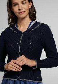 Marineblauwe gebreide cardigan met een textuurpatroon, grijze accenten, ronde kraag en knoopsluiting. Heeft decoratieve stiksels op de schouders.