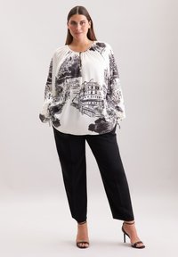 Blusa bianca con stampa architettonica nera, scollo rotondo e maniche lunghe; abbinata a pantaloni neri e tacchi neri con cinturini.