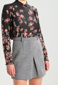 Blouse noire à fleurs rouges et blanches, assortie à une jupe grise côtelée avec une fente frontale et une taille cintrée.