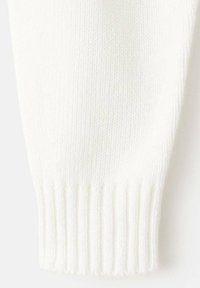 Beli pleteni manšet puloverja, ki prikazuje rebrasto teksturo, z gladko tkanino na površini in enakomerno barvo po celotni površini.