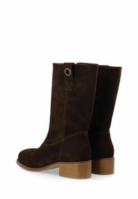 Stivaletti in suede marrone con punta tondeggiante, altezze medie e un piccolo tacco a blocco. Presentano una cintura posteriore con un accento metallico.