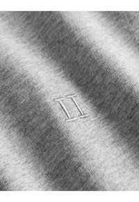 Um tecido cinza com uma textura suave apresenta um pequeno emblema bordado "II". O material parece suave e ligeiramente mesclado.
