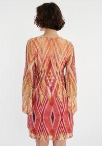 Bedrucktes Kleid mit lebhaften roten, orangen und gelben geometrischen Mustern, langen Glockenärmeln und einer lockeren Passform. Weicher, strukturierter Stoff.