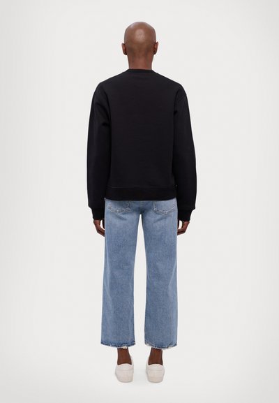 Black cotton sweatshirt with ribbed cuffs, paired with light blue wide-leg jeans and white slip-on shoes, viewed from the back.