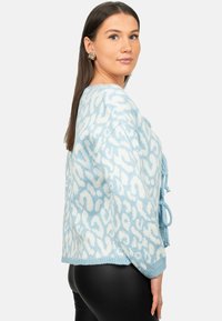 Pullover azzurro chiaro con una stampa leopardata astratta bianca, dotato di un design con nodo frontale e realizzato in un morbido materiale a maglia testurizzata.