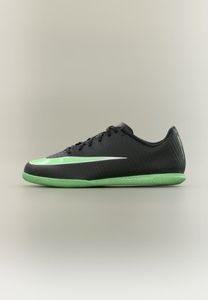 Czarny niski but sportowy z zieloną podeszwą i zielono-białym logo Nike po boku, przedstawiony na neutralnym tle.