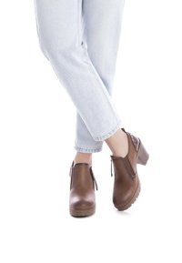 Botas de tobillo de cuero marrón con tacón ancho, cremalleras laterales y remaches decorativos, combinadas con unos jeans de corte recto en azul claro.