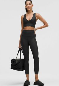 Schwarzes Sportbekleidungsset bestehend aus einem kurz geschnittenen Oberteil mit Leopardenmuster und hoch geschnittenen Leggings. Begleitet von einer schwarzen Sporttasche und einer Matte.