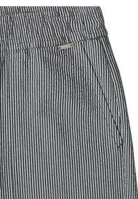 Pantalon rayé vertical noir et blanc avec ceinture élastique et poche latérale, avec une petite étiquette métallique de la marque près de la taille.