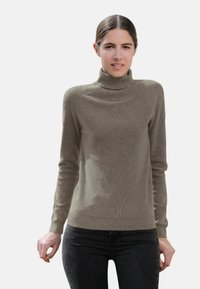 Pull à col roulé gris avec un motif en relief en forme de diamant, fabriqué à partir d'un matériau doux. Associé à un jean foncé, mettant en valeur une coupe slim et un design épuré.