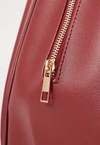 Borsa in ecopelle rossa con zip dorata e linguetta rettangolare, texture liscia e dettagli cuciti lungo la cucitura.