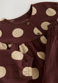 Maroon textured fabric dress with large beige polka dots, round neckline, buttoned front, and gathered elastic cuffs on long sleeves.