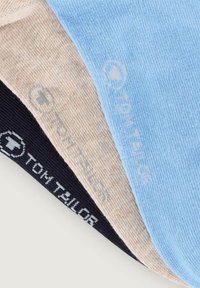 Tre sokker stablet: sort, beige og lyseblå. Hver sokke har et subtilt logo "TOM TAILOR" i en kontrastfarve på anklen. Glat tekstur.