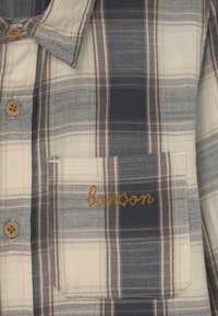 Geruite shirt met beige, marineblauwe en bruine tinten. Beschikt over een button-down kraag, houten knopen en een borstzak met "bonzon" in goud geborduurd.