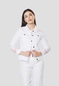 Witte spijkerjas met bloemrijke borduursels op de mouwen, knoopsluitingen, twee borstzakken en een gestructureerde kraag. Gecombineerd met witte broek.