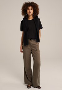 Černé tričko s krátkým rukávem, pod ním je strukturovaná černá vesta, olivové široké kalhoty a baleríny se zvířecím potiskem. Celkový vzhled doplňují jednoduché doplňky.