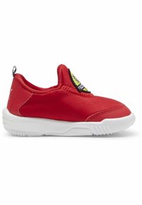 Piros vászon slip-on cipő fehér gumitalppal, egy kör alakú sárga folttal és fekete díszítéssel a sarkán. Az anyag sima tapintású.