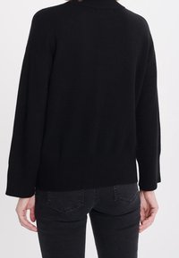 Czarny dzianinowy sweter z wysokim kołnierzem, opuszczonymi ramionami i ściągaczem u dołu. Połączony z ciemnymi dżinsami. Gładka tekstura, swobodny fason.