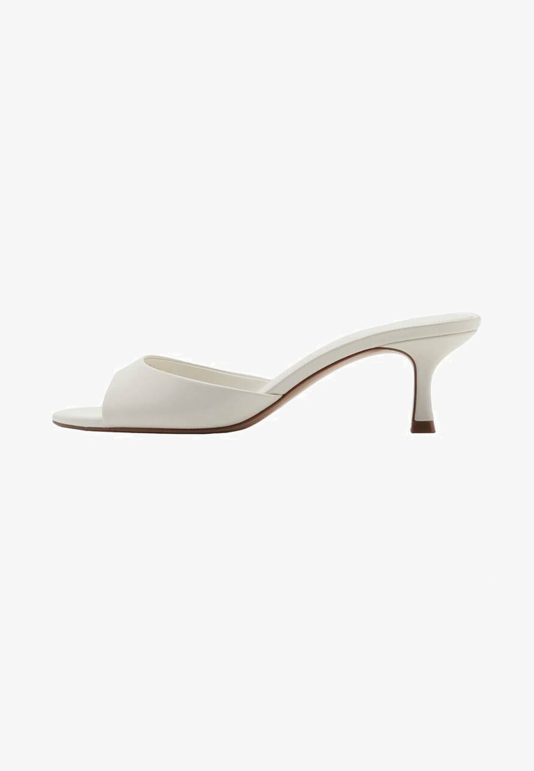 Mules à talons hauts ouverts et blancs avec une finition lisse, un design minimaliste et un talon fin, mettant en avant un accent brun subtil sur la semelle.