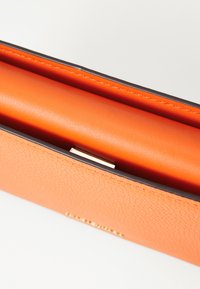 Orange läderclutch med en texturerad utsida, med en slät orange foder och ett spänne i guld.