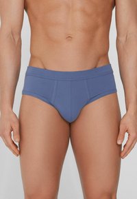 Pánské slipy v měkké modré látce, s širokým páskem, tvarovanou přední kapsou a hladkým povrchem.