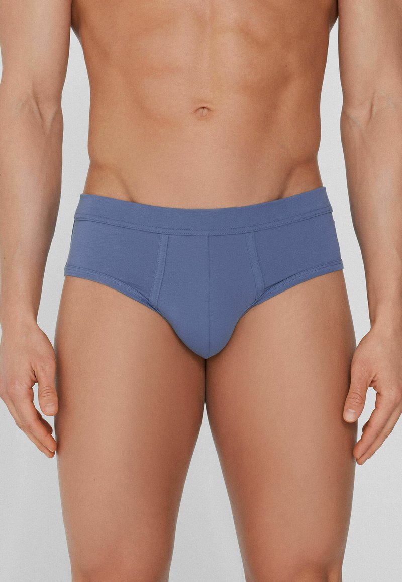 Pánské slipy v měkké modré látce, s širokým páskem, tvarovanou přední kapsou a hladkým povrchem.
