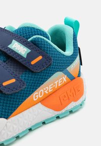 Sportskor med en överdel i tyg i blått, med orangea detaljer och GORE-TEX-logotyp. Säkert grepp med kardborreband och en texturerad vit sula.