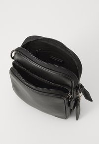 Borsa in pelle nera con forma rettangolare, caratterizzata da tre scomparti con zip, superficie testurizzata e dettagli hardware decorativi.