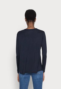 Marineblaues Langarmoberteil mit rundem Ausschnitt, weicher Textur und lockerer Passform, kombiniert mit blauen Jeans, von hinten sichtbar.