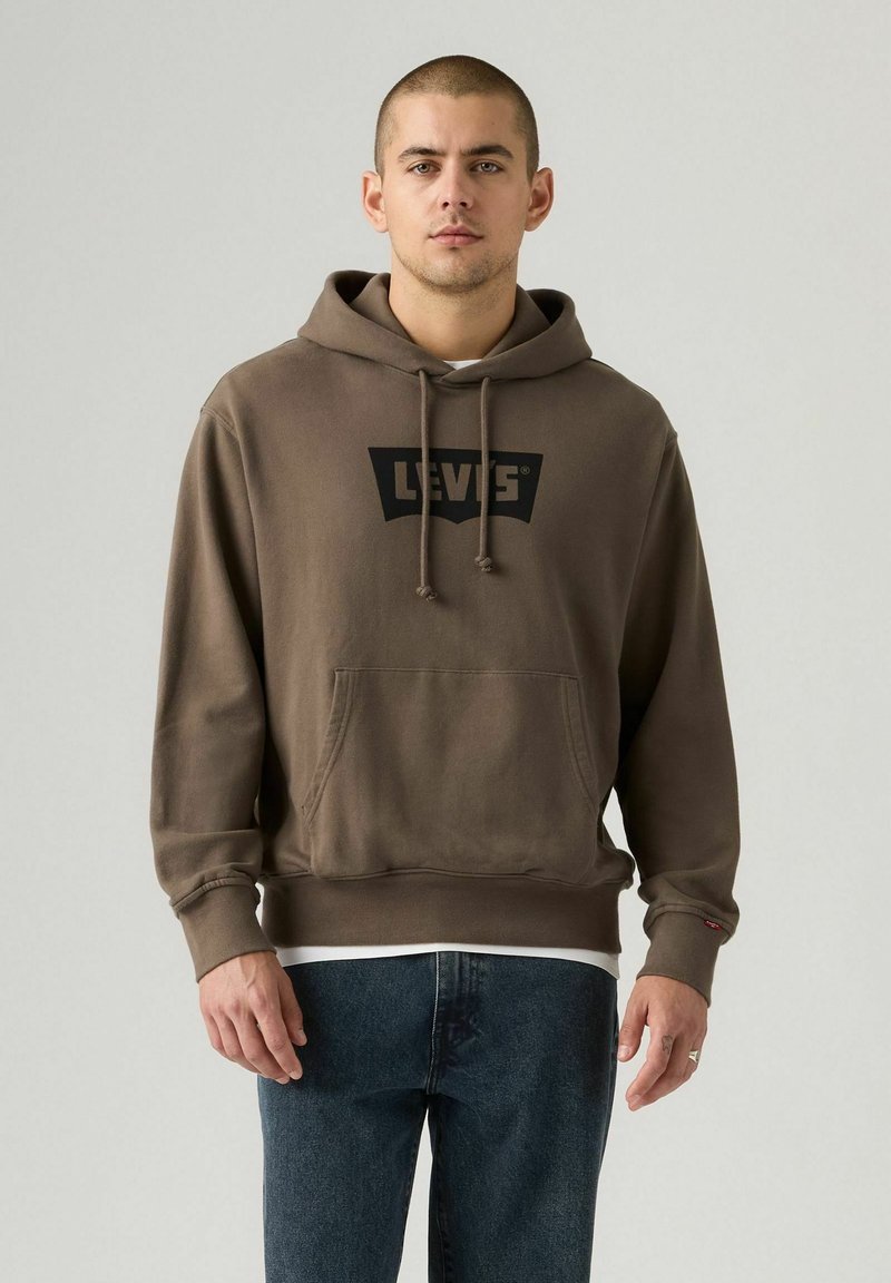 Sudadera marrón con un gran logo negro de Levi's. Cuenta con un bolsillo frontal tipo canguro, capucha con cordones y puños acanalados. Se lleva con jeans de mezclilla oscura.