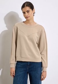 Felpa beige con maniche lunghe, scollatura rotonda, borchie decorative lungo le spalle e il petto, tessuto morbido, vestibilità regolare e orlo a coste.