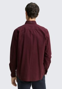 Chemise à carreaux bordeaux à manches longues, avec des poignets boutonnés et un motif subtil. Présente un col classique et un détail de bouton à l'arrière.