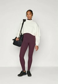 Lühendatud kreemivärvi pusakas, kõrge vöökohaga burgundi värvi retuusid, mustad jooksukingad ja must kott. Pehme materjal, figuuri jälgiv disain, minimaalne kaunistamine.