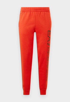 Pantaloni da ginnastica rossi realizzati in tessuto morbido, con vita elastica, tasche laterali e testo del logo nero lungo la gamba sinistra.