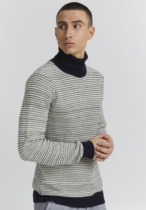 Strikket turtleneck-genser i krem og marineblå med et teksturert sik sak-mønster, ribbede mansjetter og en tettsittende silhuett.
