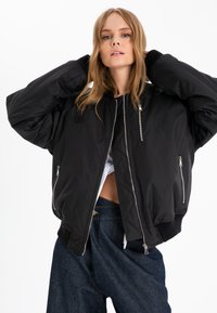 Black bomber jacket with ribbed cuffs, two front zip pockets, and a quilted lining. Features a zip front and minimalistic design.