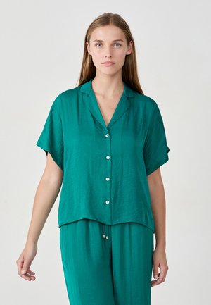 Chemise boutonner à manches courtes en teal, fabriquée en tissu léger, avec un col en V et une coupe décontractée. Texture lisse, détails minimaux.